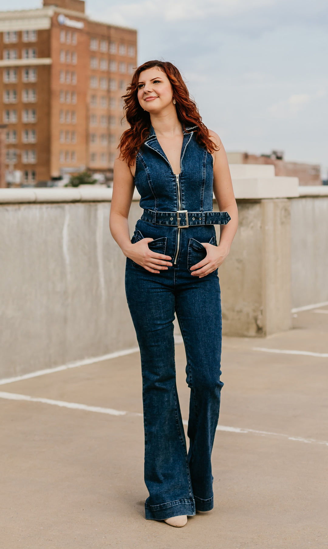 Denim sleeveless jumpsuit with zipper front, flared legs, and belt